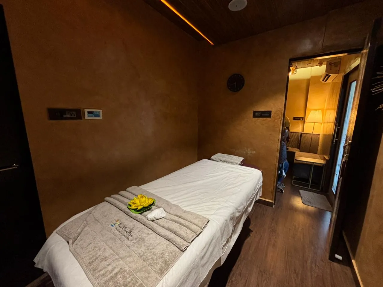 A Sector 7 treatment room, bed dressed with folded towels and a lotus, warm lamplight through the doorway beyond